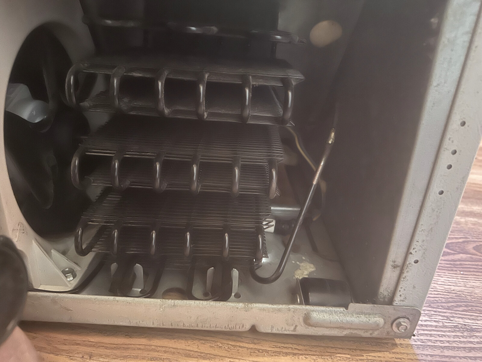 Cleaned refrigerator condenser coils on a hardwood floor after dust and pet hair removal during an appliance service call