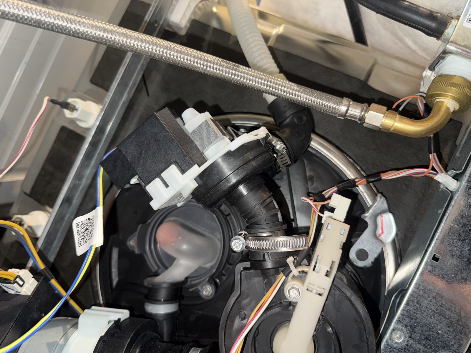 Dishwasher drain pump assembly with hose connections and water supply line photographed during a real repair
