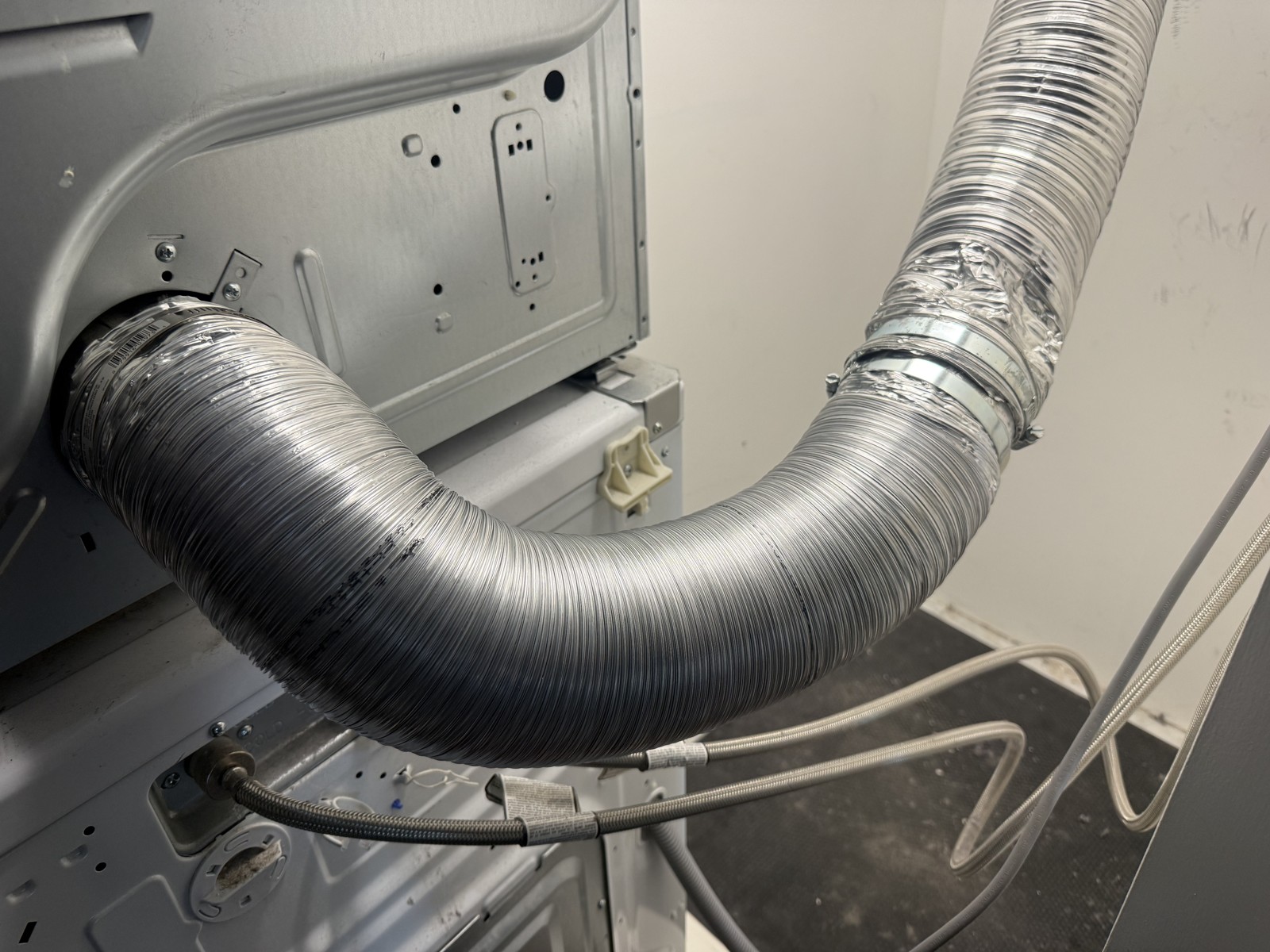 Semi-rigid aluminum dryer vent duct connected at the back of a dryer, photographed during a vent cleaning service call