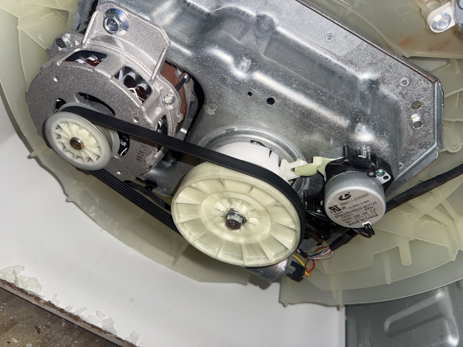 Belt-driven washer drive system showing the motor, pulley, transmission and start capacitor during a repair