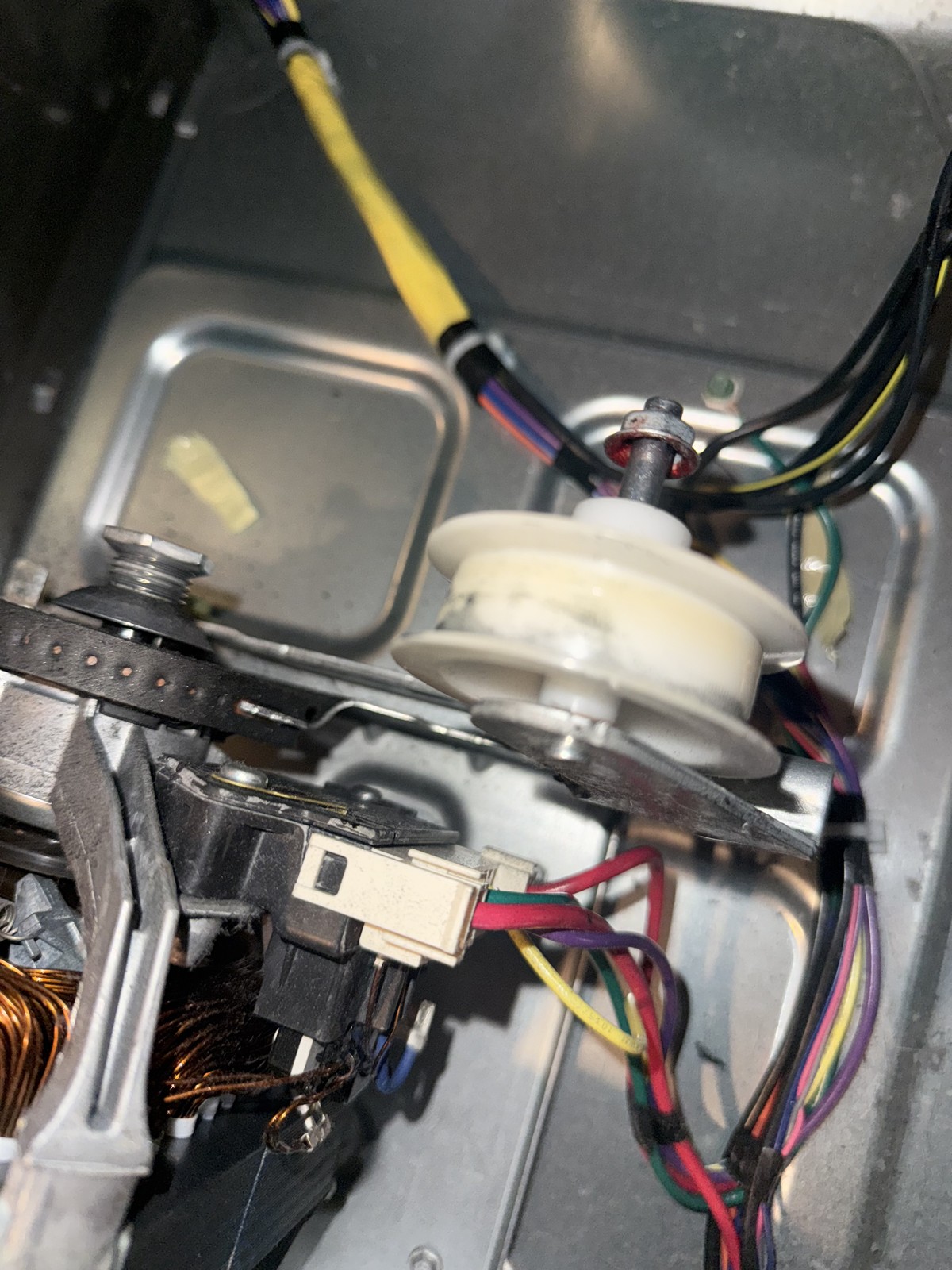 Washer drive belt and pulley assembly during a replacement repair, photographed on the floor next to the machine